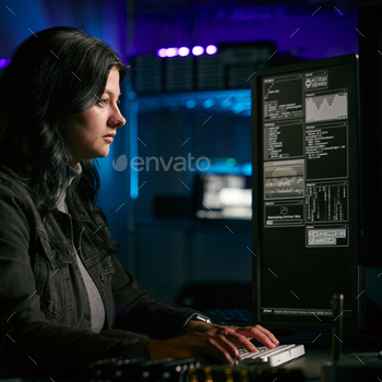 Low Key Lighting Shot Of Female Computer Hacker Sitting In Front Of Screens Breaching Cyber Security