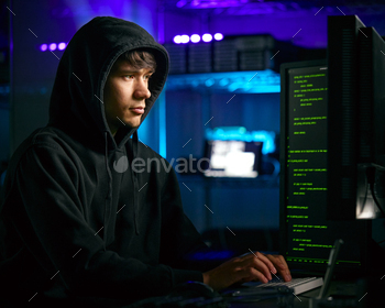Low Key Lighting Shot Of Male Computer Hacker Sitting In Front Of Screens Breaching Cyber Security