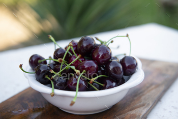 White plate, board of wet cherries, merries laying on wooden board, table outdoors.