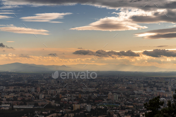 a city below the cloudy sky in the middle of sunset