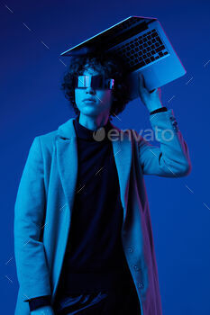 Portrait of a stylish male hacker with a laptop and futuristic glasses in blue light, cyber security