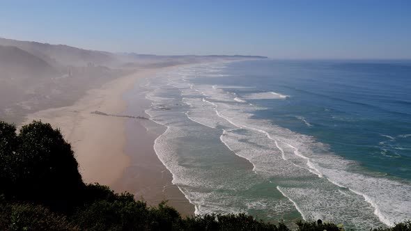 View from mountain over wide stretch of gorgeous beach with waves rolling on to it.