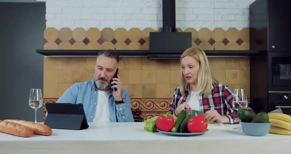 Woman Cutting Cucumber for Vegetable Salad while Her Handsome Husband Talking on Phone