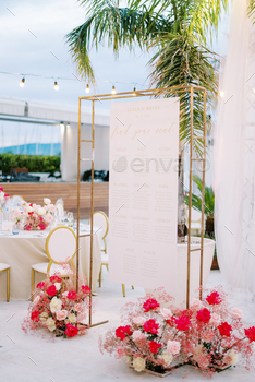 Seating plan hangs on a rectangular frame next to bouquets of flowers in front of the set festive