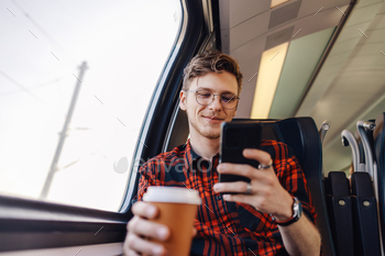 A man is traveling by train and typing messages on the phone.