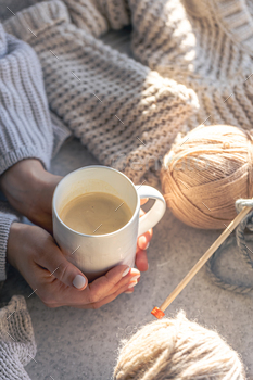 A cup of coffee in female hands and a thread of yarn.