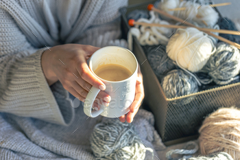 A cup of coffee in female hands and a thread of yarn.