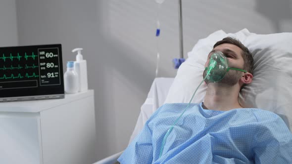 The Man Lies on the Bed in the Hospital in Oxygen Masks and Regains Consciousness
