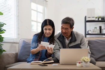 Asian senior couple checking and calculate financial bill together on sofa involved in financial