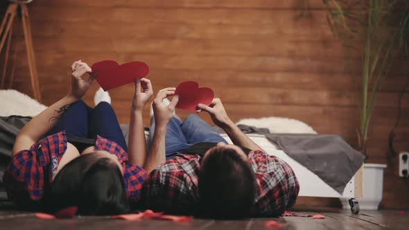 couple in love are playing with handmade hearts in their hands on the bed on St. Valentine's Day
