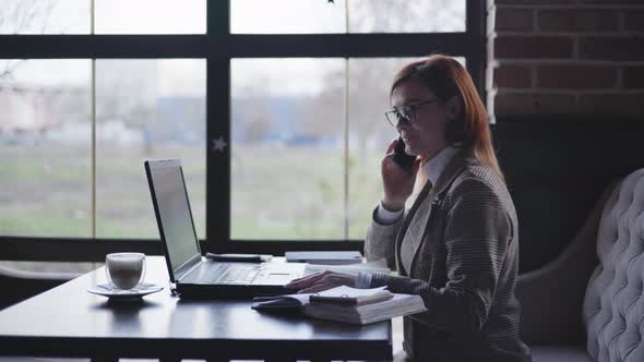 Young Beautiful Successful Woman in Glasses for Vision Speaks on Phone with Business Partner and