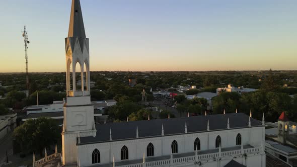 Aerial view flying beside church bell tower on a small town at golden hour