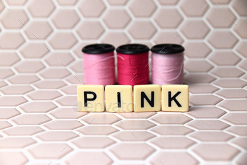 three bobbins with pink thread behind the word pink on pale pink background