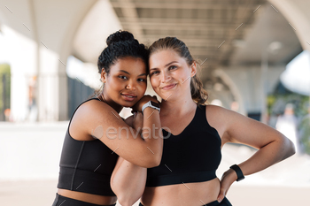 Two young smiling women with similar body types hugging each other after a workout.