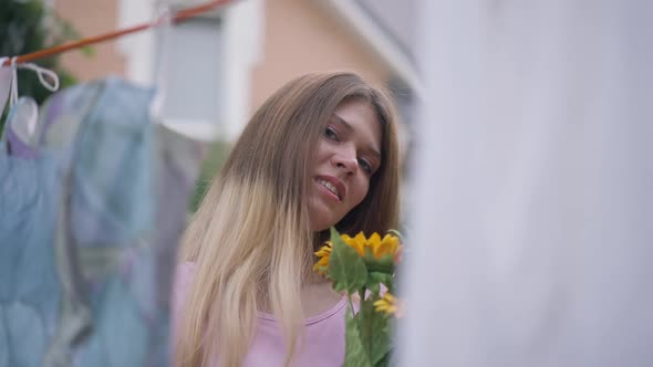 Slim Charming Woman Posing with Bouquet of Sunflowers Outdoors As Clean Laundry Hanging at Front