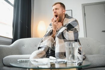 unhappy sick man spraying his throat with oral spray in bed at home.