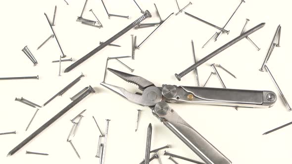 Metal Round-nose Pliers Among Nails on White, Rotation