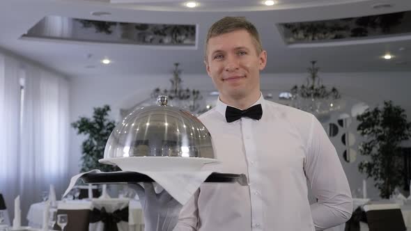 A Male Waiter Holds a Tray with a Covered Dish in a Restaurant