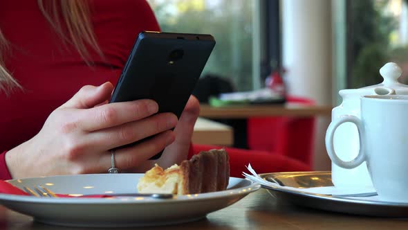 A Woman Sits at a Table with Meal in a Cafe and Works on a Smartphone - Closeup