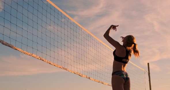 Athletic Girl Playing Beach Volleyball Jumps in the Air and Strikes the Ball Over the Net on a