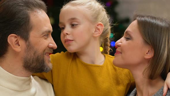 Girl Kissing Mom and Dad on Cheeks, Showing Love and Care to Family on Christmas