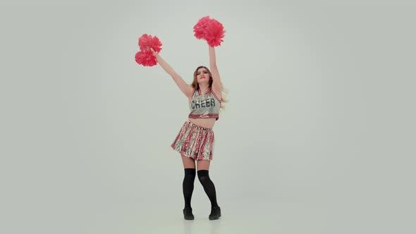 Young Cheerleader with Red Pompoms in Uniform is Dancing on White Background in Studio