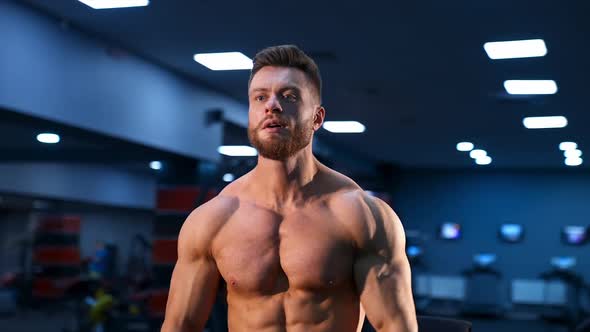 Athletic man in gym is posing to the camera. Bodybuilder with perfect body. 