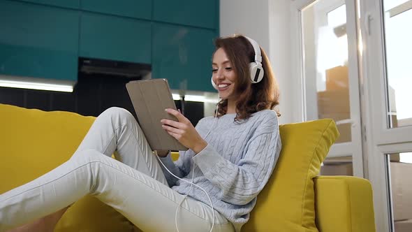 Girl with Wavyhair Sitting with Laptop on the Cozy Sofa and Listening Music