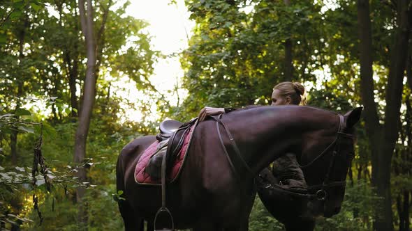 Female Equestrian Climbs on Horseback with Help of Stirrup During Sunny Day in the Forest