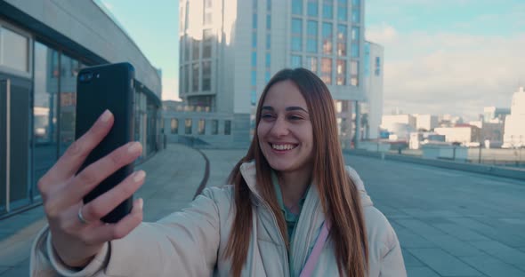 Cheerful Attractive Ginger Woman Talking By Videocall on Smartphone and Waving at Camera in the City