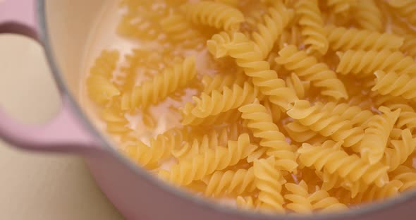 Fusilli in bowl with water pouring for cooking