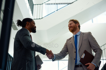Below view of happy businessmen handshaking in a hallway.