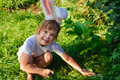 Child girl in a headband with bunny ears is looking for Easter eggs in the grass. - PhotoDune Item for Sale