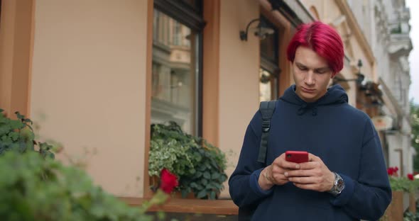 Crop View of Young Man in Casual Clothes Using Smartphone While Standing Near Cafe at Street