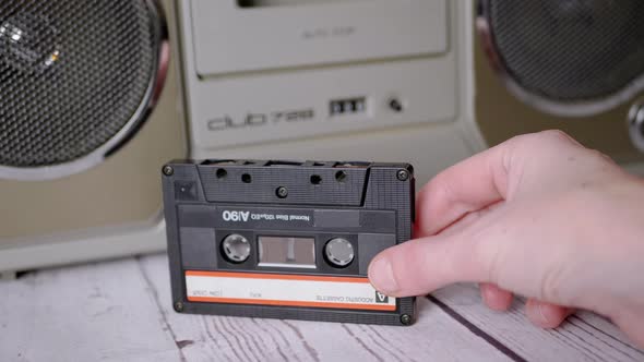 Female Hand Holds an Old Audio Cassette From the 90s Near a Stereo Tape Recorder