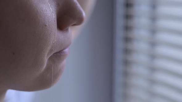 unrecognizable woman is crying near the window, a tear is rolling down her cheek