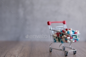 A shopping cart overflowing with colorful pills on a wooden table.