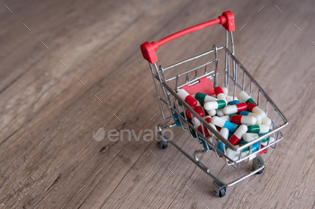 A shopping cart overflowing with colorful pills on a wooden table.