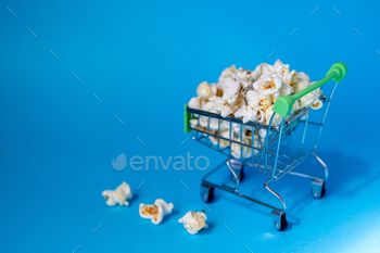 Freshly made popcorn in a shopping cart on blue background