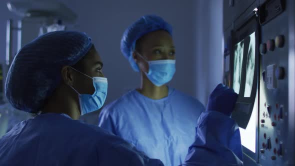 Mixed race female surgeons wearing protective clothing looking at x-ray on screen