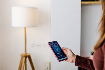 Young woman using smart home application on cell phone at home
