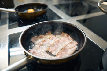 Premium quality bacon fried in a frying pan
