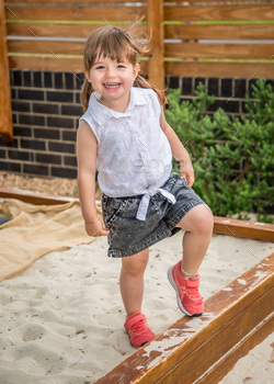 small girl standing on one leg in a sandbox playing outside