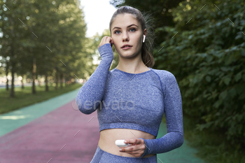 Woman in sportswear on track applying earphones