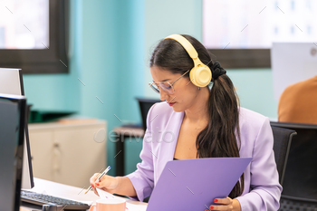 Concentrated woman with headphones and documents.