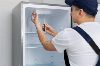 Man in a uniform repairs the light in the refrigerator with a screwdriver. Replacing the light bulb.