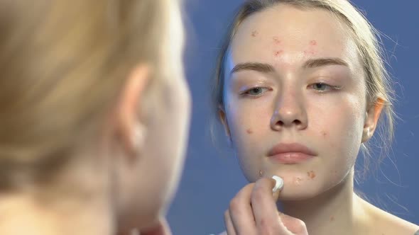 Female Teenager Applying Cosmetic Treatment on Face Pimples