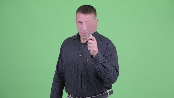 Macho Mature Businessman As Detective Inspecting with Magnifying Glass