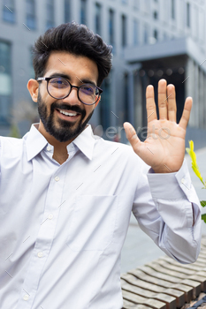Cheerful businessman waving hello outdoors, friendly corporate professional greeting