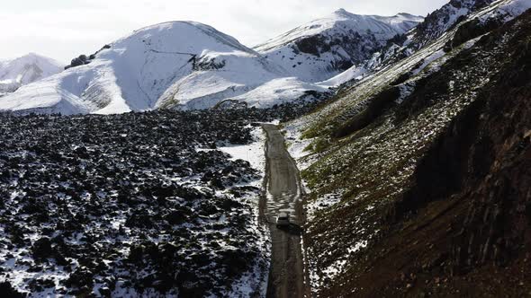 Aerial of Car Driving on Dirt Road Along the Snow Covered Mountains in Iceland